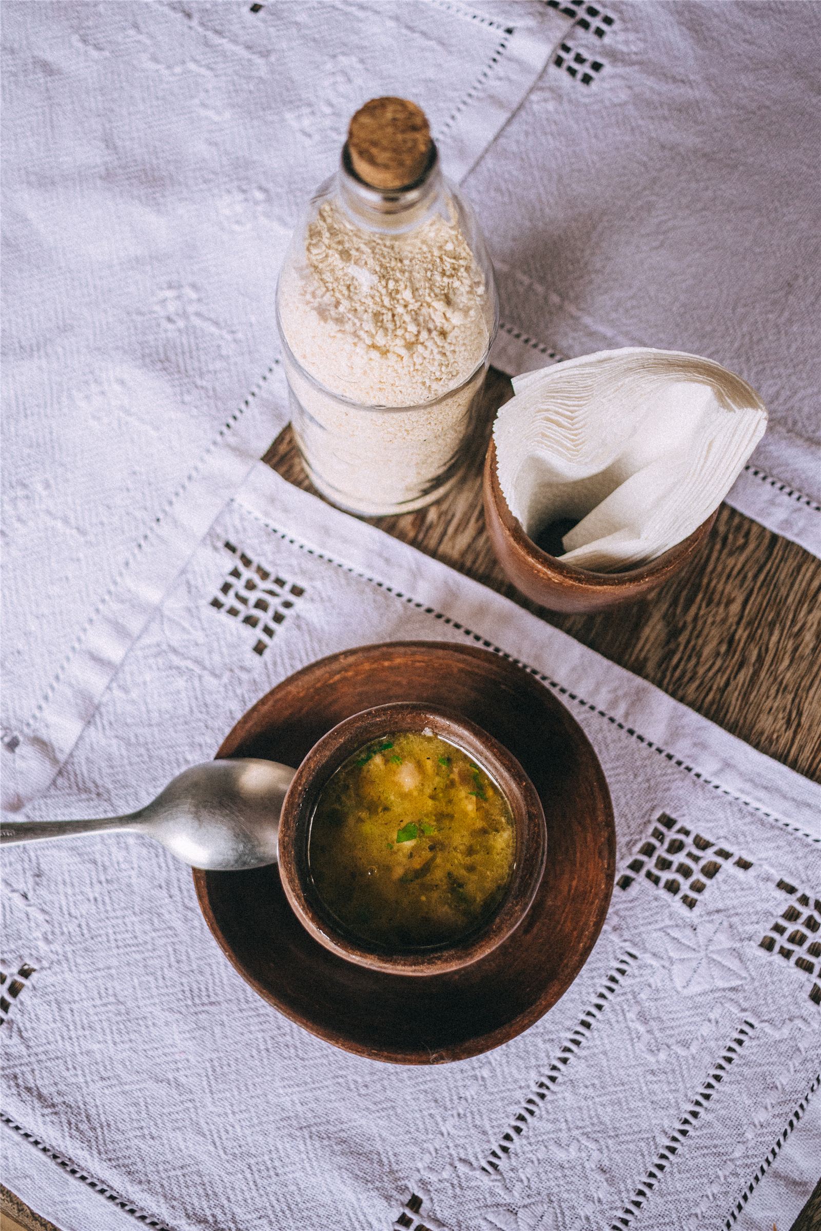 Caldo servido em tigela de barro com farinha, sobre toalha bordada do Gracinha